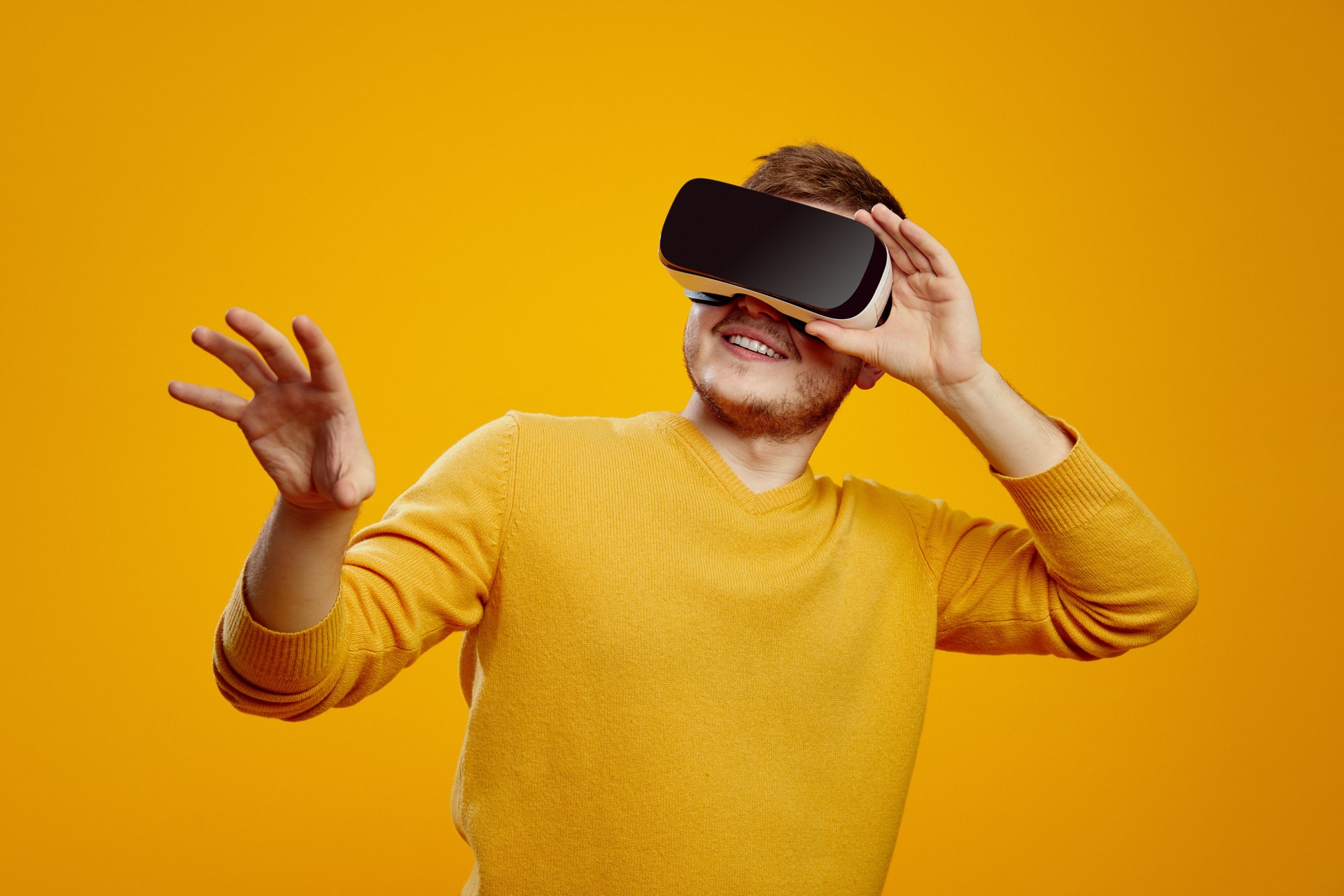 Casual bearded man wearing yellow sweater trying VR headset and exploring another world